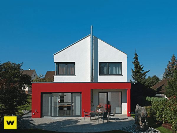 Modernes Einfamilienhaus mit roter Fassade, Flachdach und großem Garten bei Sonnenschein.