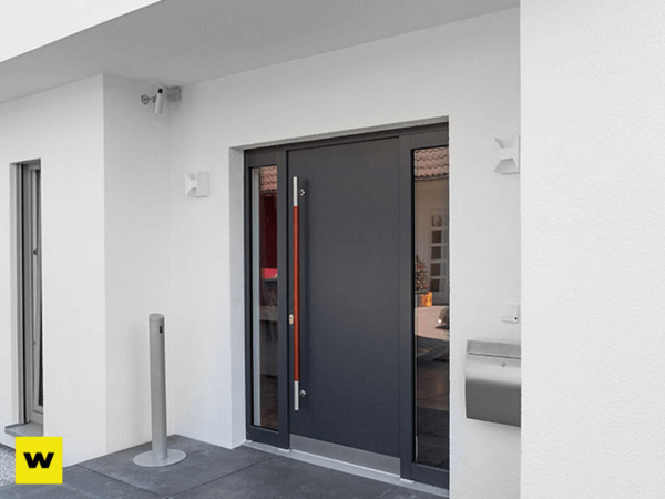 Moderne Haustür aus Aluminium mit Glaselementen und Edelstahlgriff an weißer Fassade.